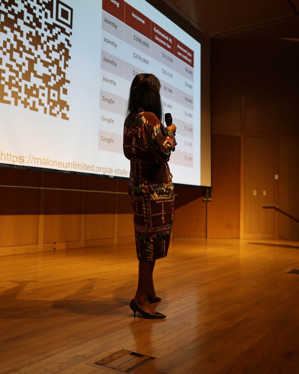 A speaker presenting on stage in front of a screen